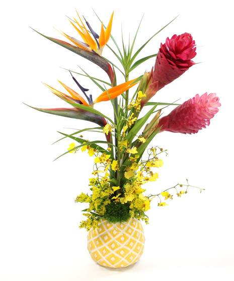 a vibrant tropical arrangement featuring bold stems of ginger & a variety of tropic flowers including oncidium orchids, birds of paradise & more in a whimsical pineapple vase