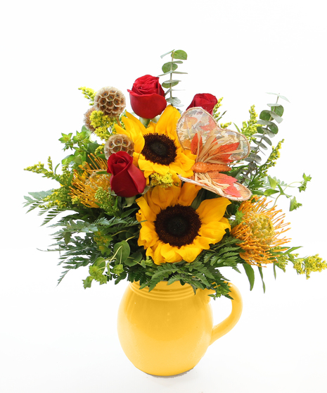 Brighten your space with this charming bouquet of sunflowers, pin cushion protea, and accents, all nestled in a simple white ceramic pitcher.