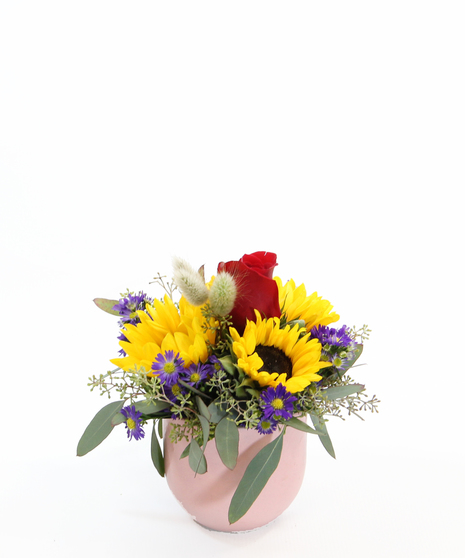 A charming mix of yellow mini sunflowers, soft bunny tail grass, seeded eucalyptus, and spring asters arranged in a simple ceramic pot,