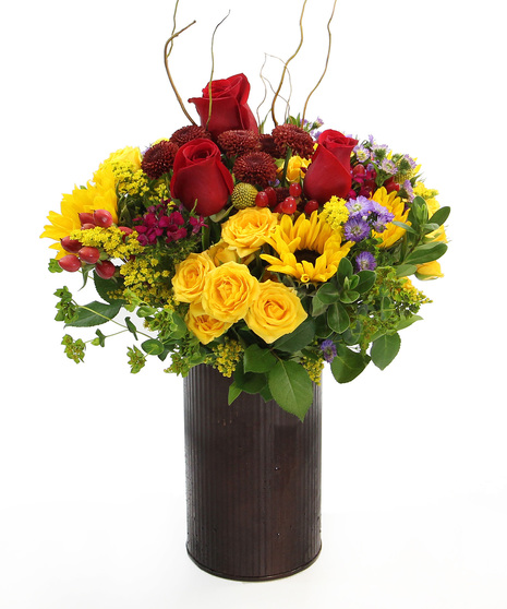 Radiant sunflowers, spray roses, and fall poms and accents in a  burnt copper cylinder.